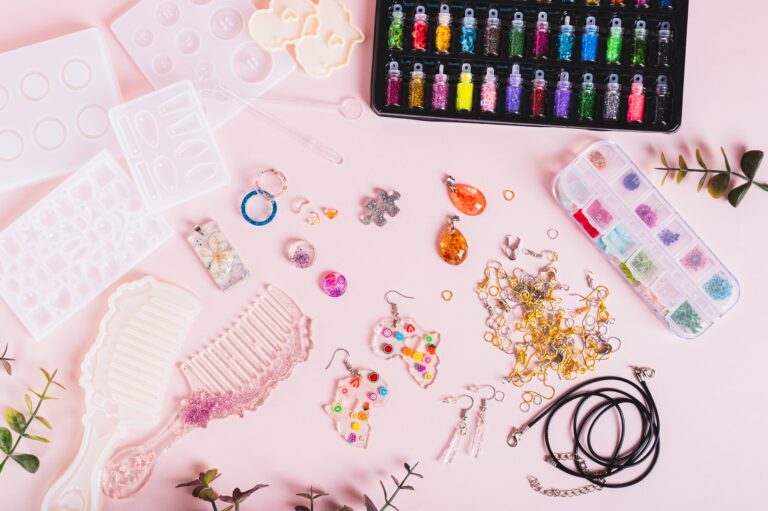 Epoxy resin jewelry and comb, molds and glitter on pink background top view